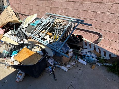 Pile of broken furniture, a bin and bottles against a block wall